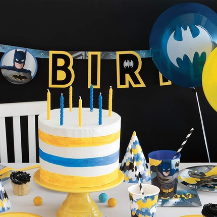 Birthday cake with candles, Batman-themed balloons, and party decorations on a table.