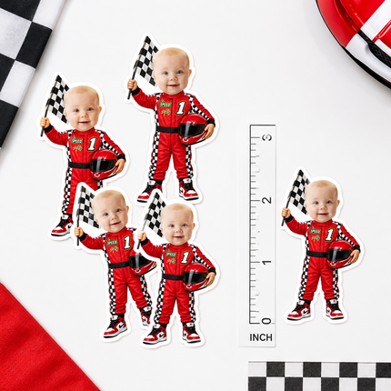 Five die-cut baby racecar stickers featuring a toddler in a red racing suit holding a checkered flag, shown on a white background with a ruler for scale and racing-themed corner props.