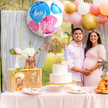 Pregnant couple at a gender reveal party with balloons and cake.