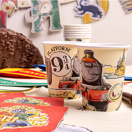 Two paper cups with Harry Potter-themed designs on a table with party decorations.