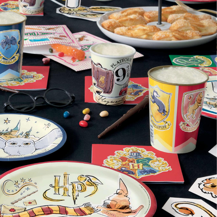 Table setting with Harry Potter-themed cups, plates, and snacks on a dark surface.