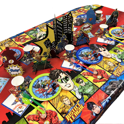 Superhero-themed party tableware including plates, cups, and napkins on a red tablecloth.