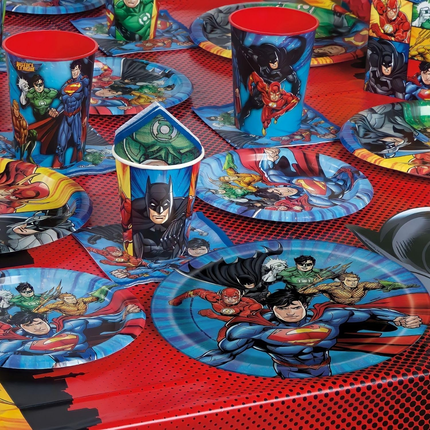 Superhero-themed tableware including cups and plates on a red surface.