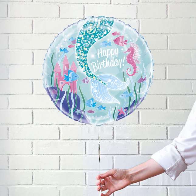Round birthday balloon with undersea design and 'Happy Birthday!' text on a white brick wall background.