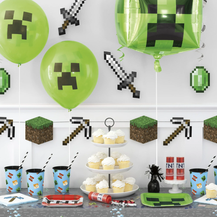 Minecraft-themed party setup with balloons, cupcakes, and decor on a white wall.