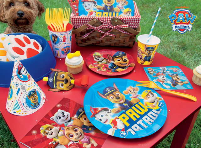 Paw Patrol-themed party supplies including plates, cups, and utensils on a red table outdoors